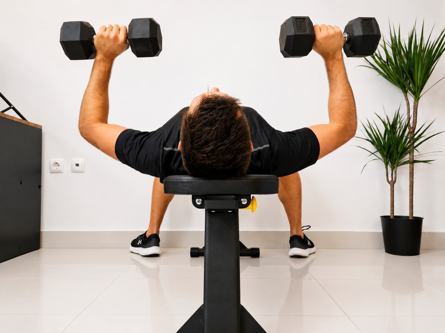Fitness model doing dumbbell bench press on the MightyRock weight bench in home gym